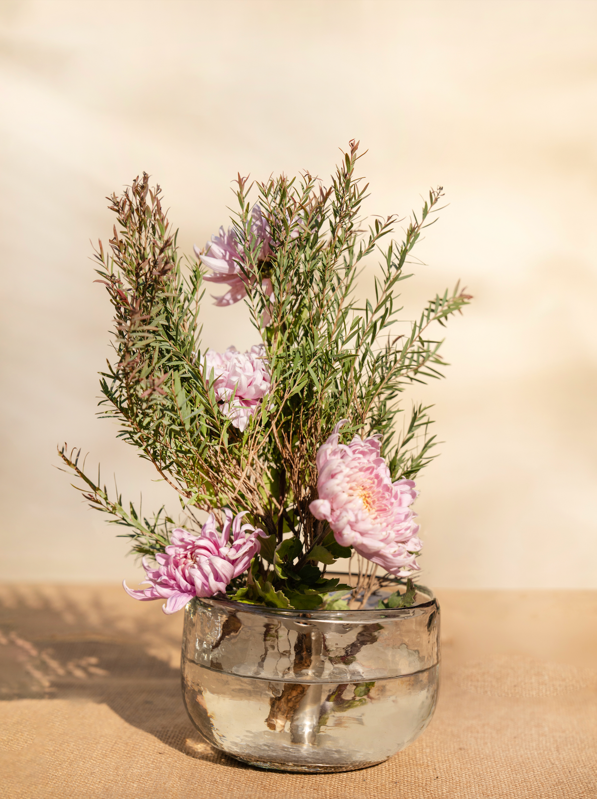 Low metal flower frog holder with pink blossoms and green stems in a round cup