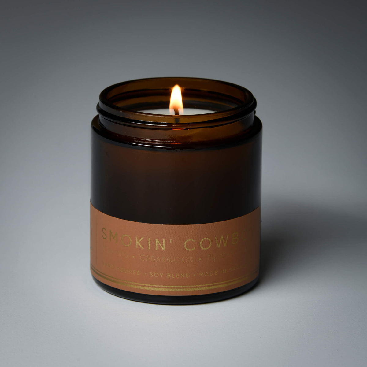 Brown glass candle jar with burning wick and 'Smokin' Cowboy' label