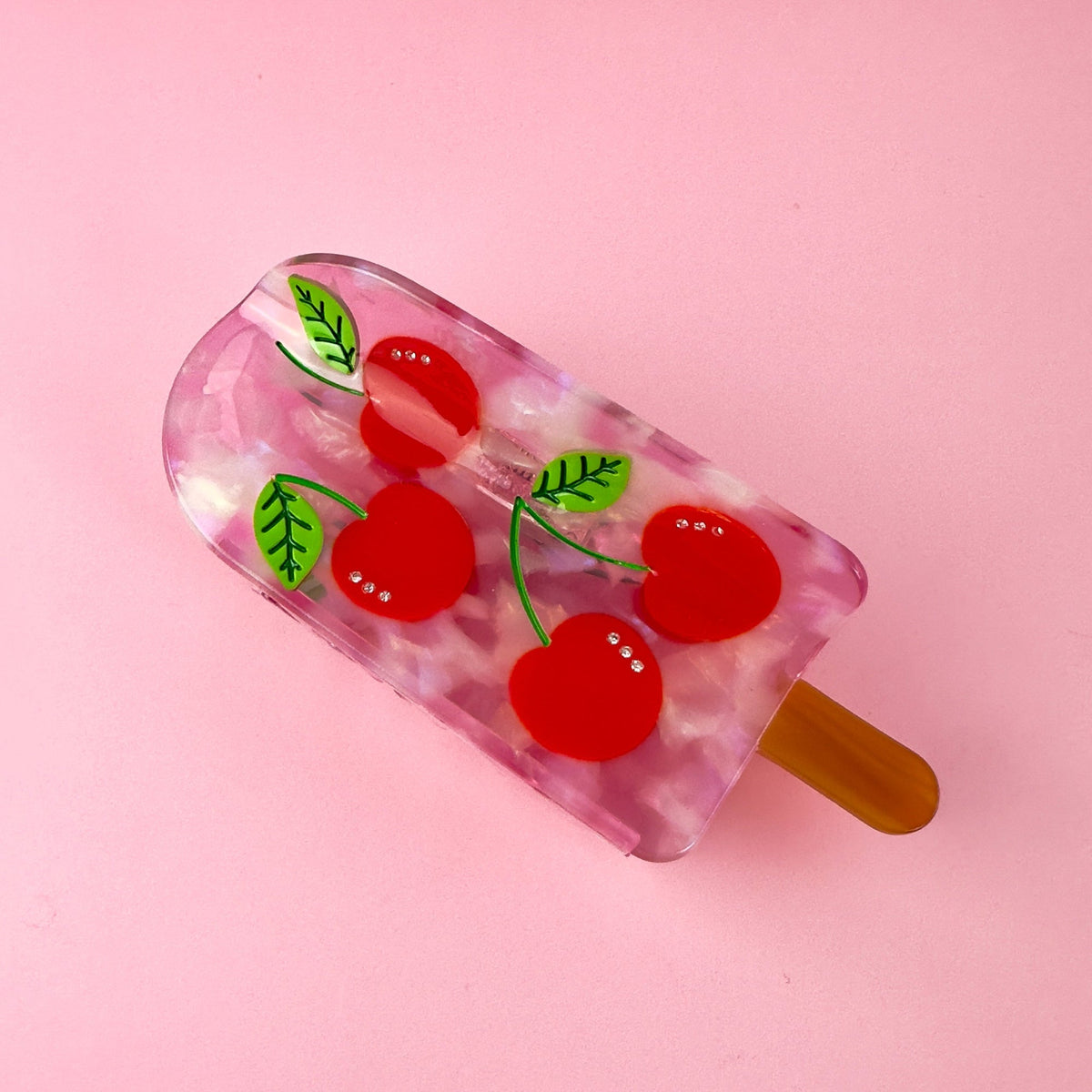 Cherry popsicle hair claw featuring translucent pink body, red cherries, and tan side handle