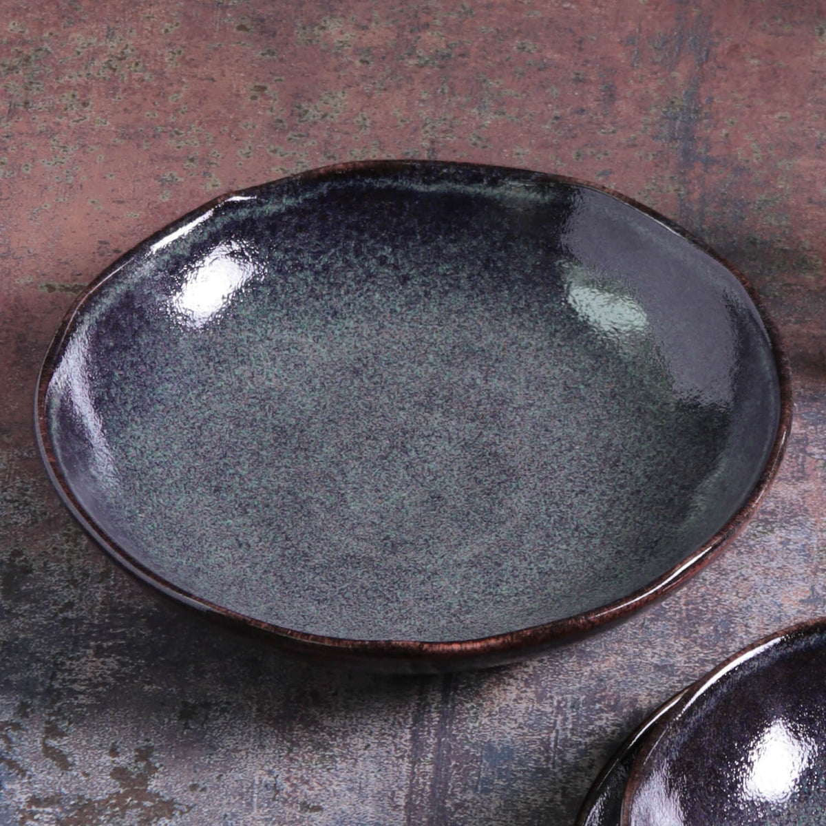 Dark speckled ceramic pasta plate with glossy finish; second plate edge visible.