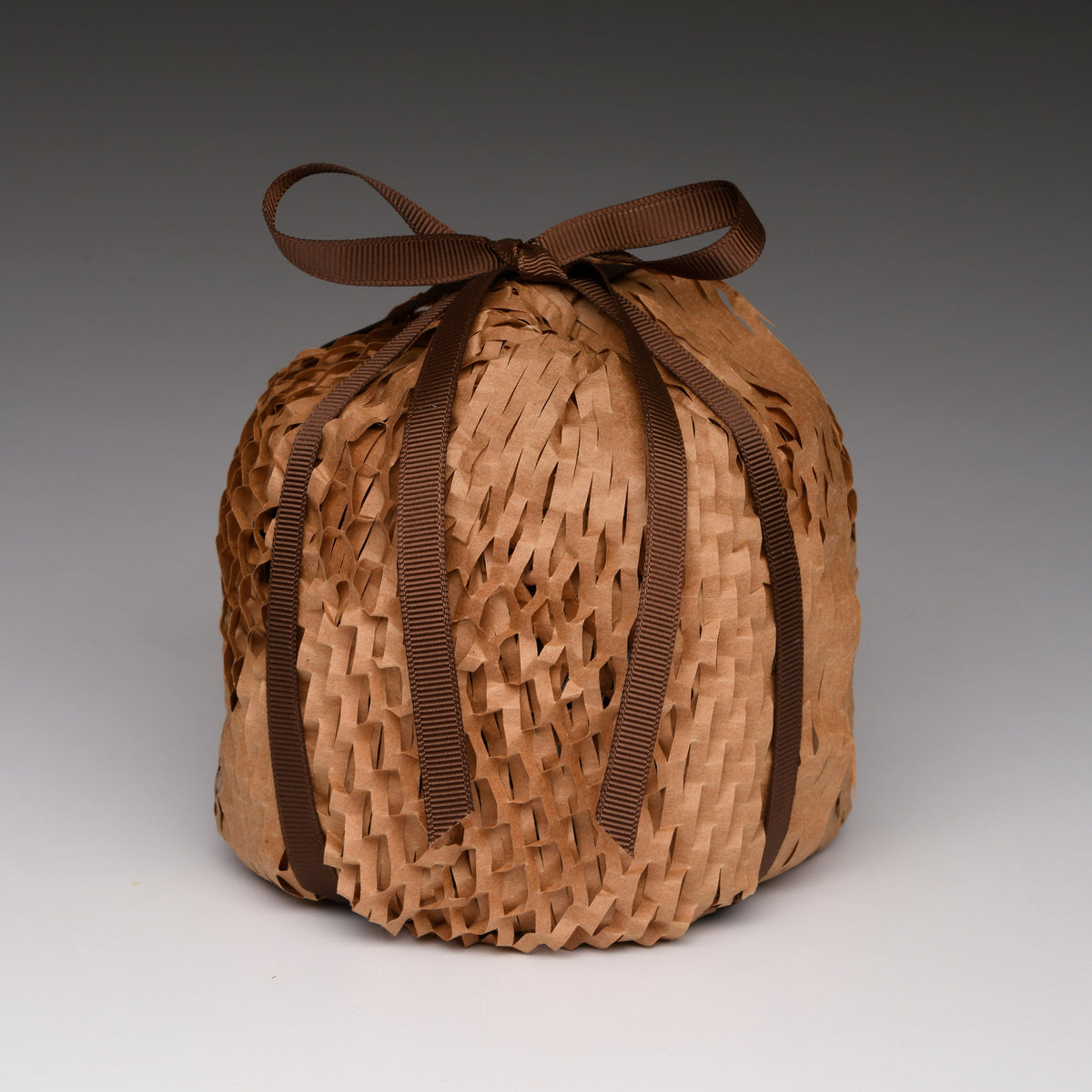 Wrapped woven candle container tied with dark ribbon, warm light brown.