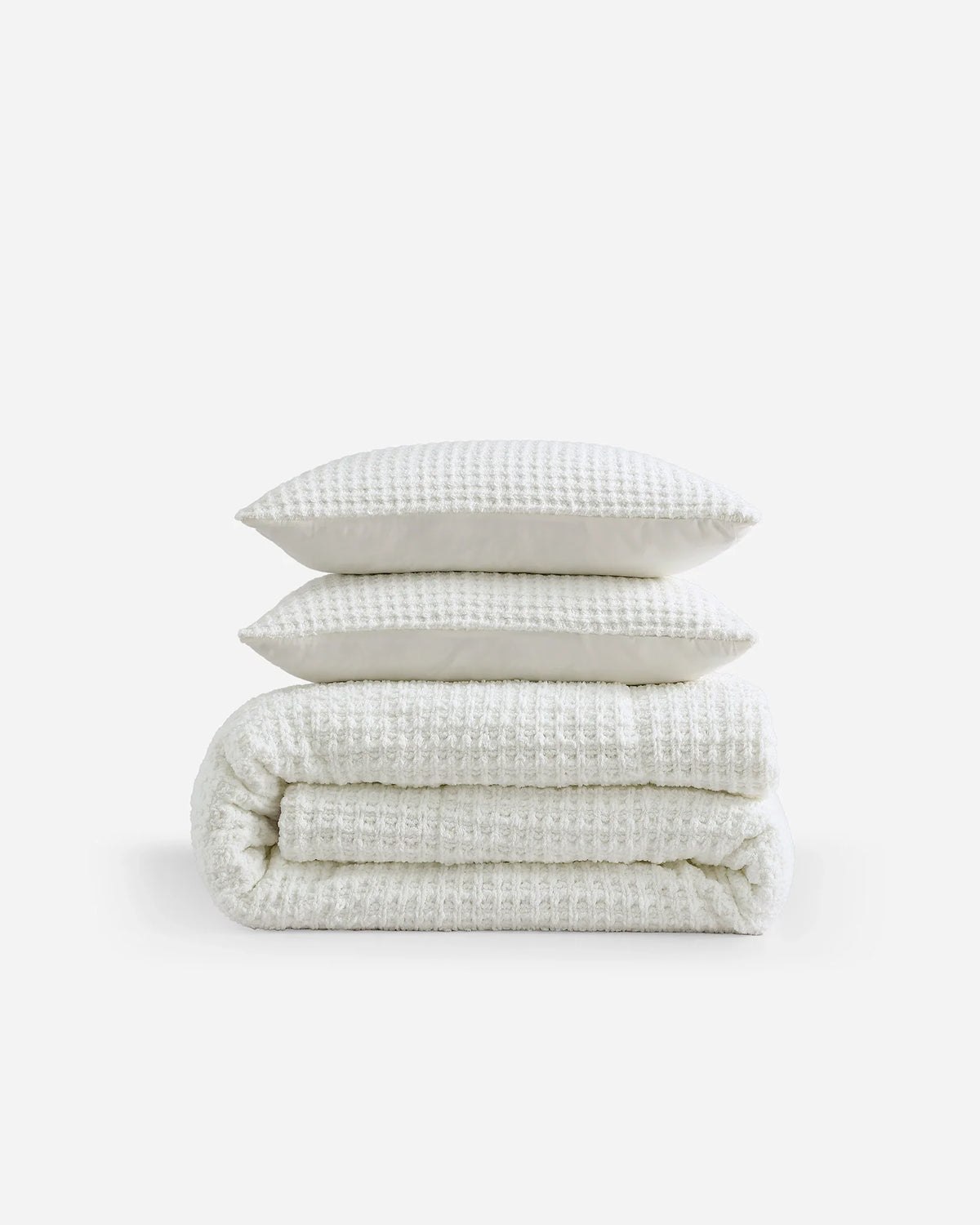 Off-white waffle comforter with two matching textured pillows, neatly stacked