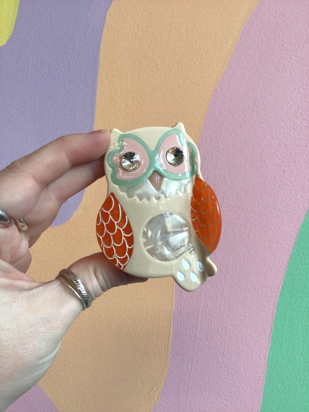 Owl hair claw with white body, orange wings and teal details, claw-shaped grip