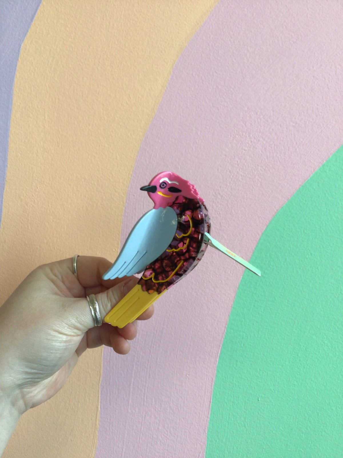 Pink and teal bird hair claw with colorful feather pattern and yellow beak