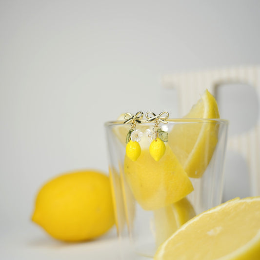 Pair of lemon dangle earrings with yellow lemon drops, green leaves, and gold hooks