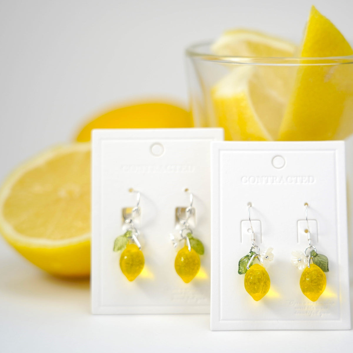Two pairs of lemon dangle earrings on cards with yellow charms and green leaf accents