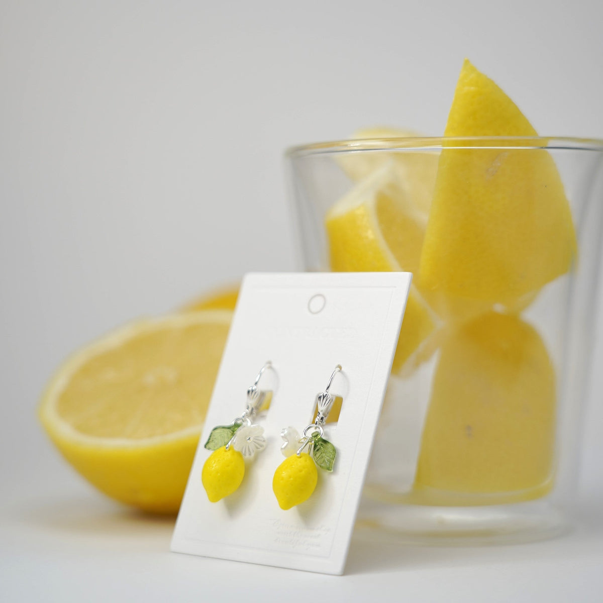Silver hook lemon dangle earrings with flower and green leaf charms on display card