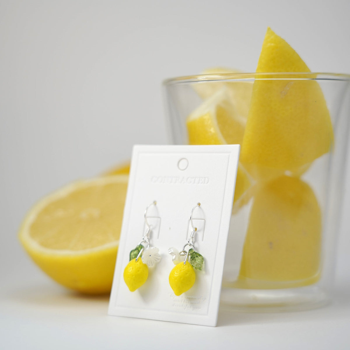 Silver lever-back lemon dangle earrings with flower and green leaf charms on display card
