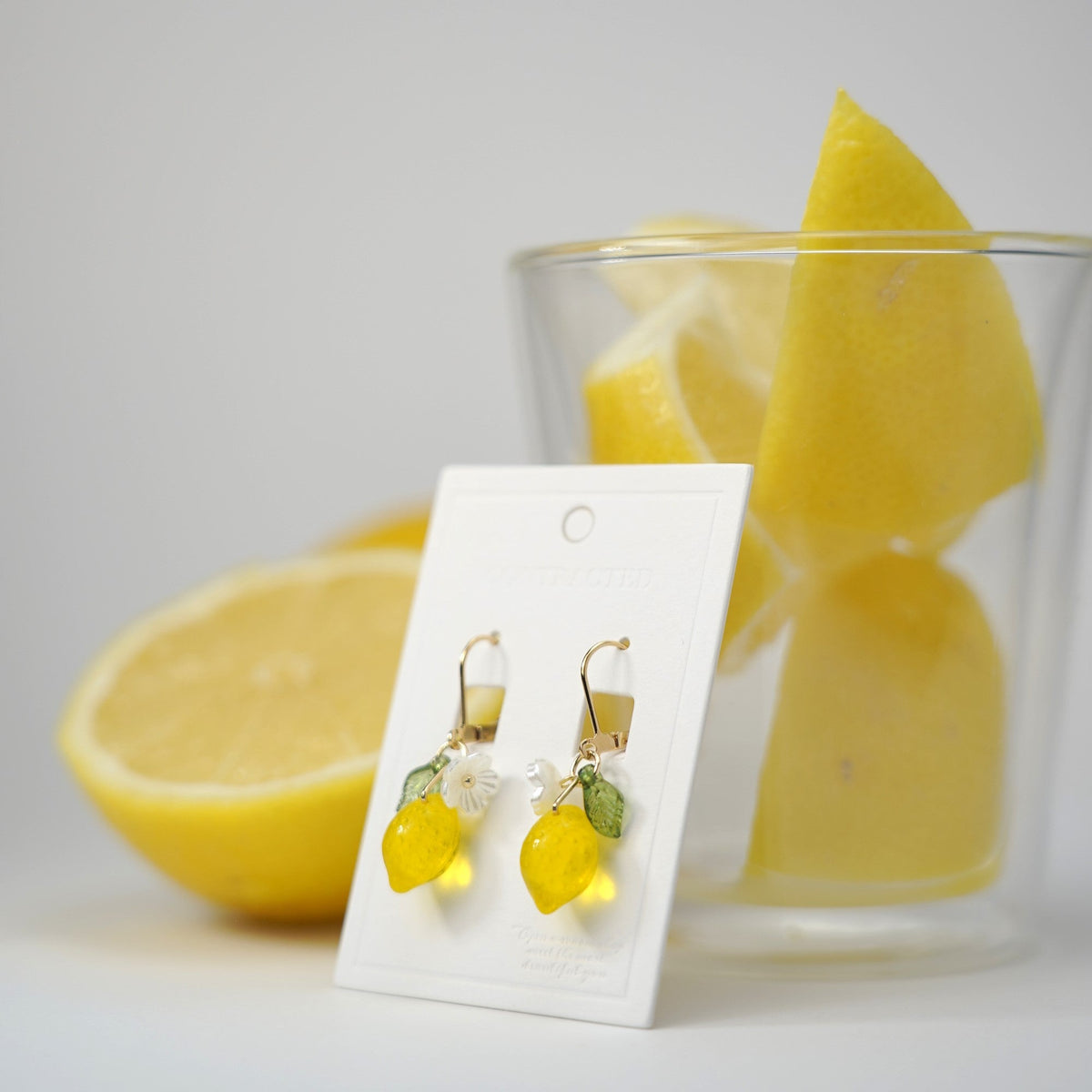 Gold bowtie stud lemon dangle earrings with flower and green leaf charms on display card