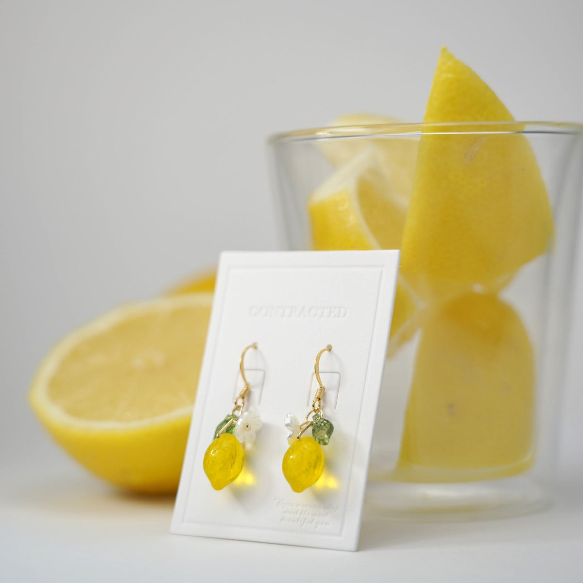 Gold hook lemon dangle earrings with flower and green leaf charms on display card