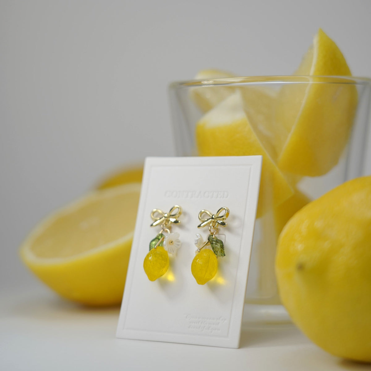 Gold bowtie stud lemon dangle earrings with flower and green leaf charms on display card