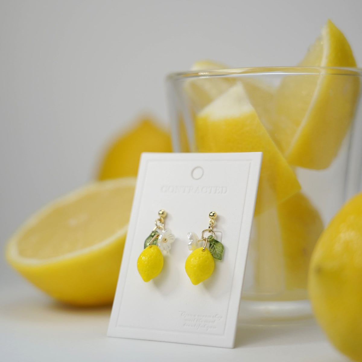 Lemon dangle earrings with gold hooks, flower and green leaf charms on display card