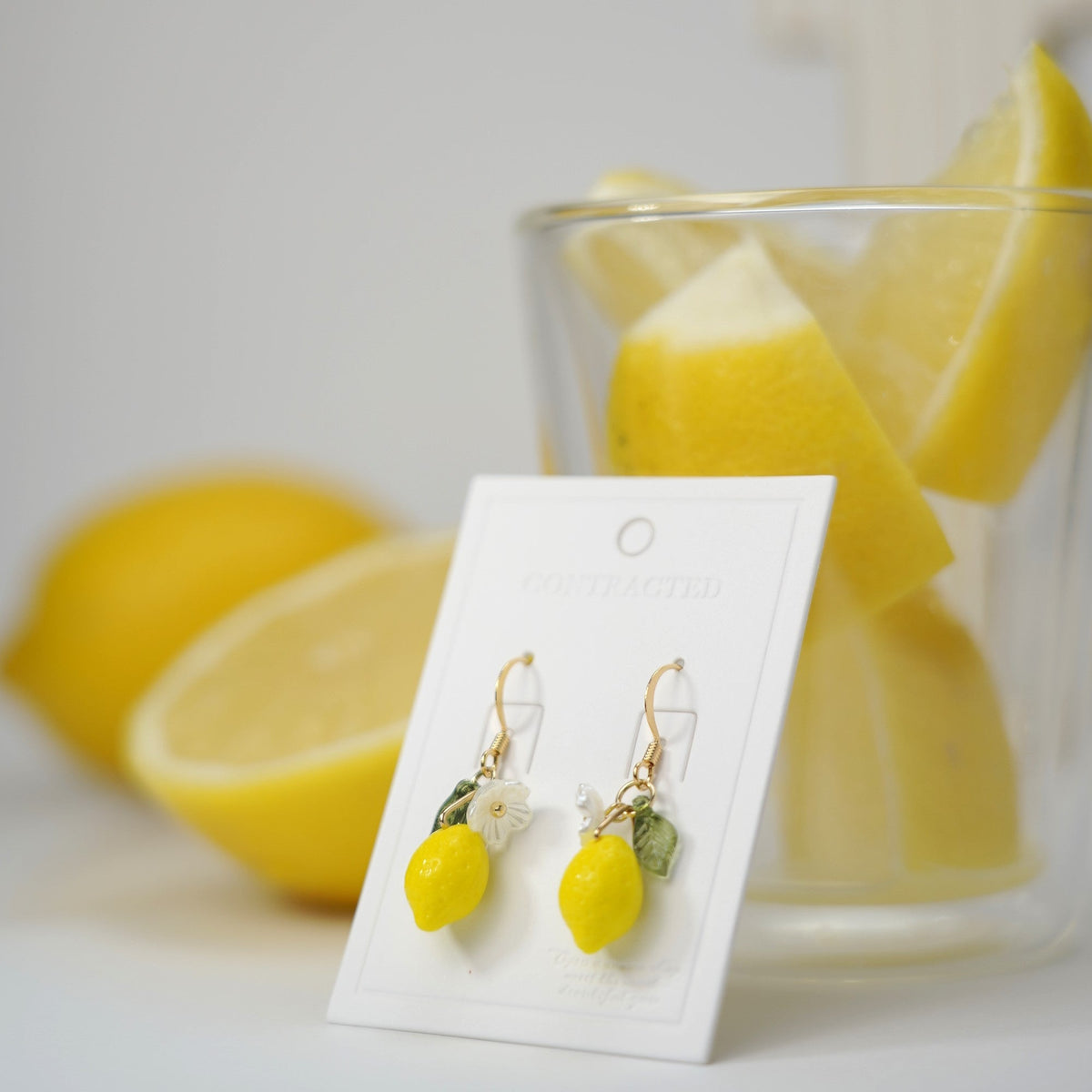 Lemon dangle earrings with silver hooks, flower and green leaf charms on display card