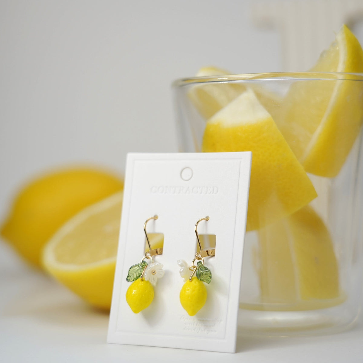 Lemon dangle earrings with gold lever-back findings, flower and green leaf charms on card