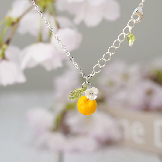 Silver fruit necklace with orange charm, green leaf, and white flower pendant on chain