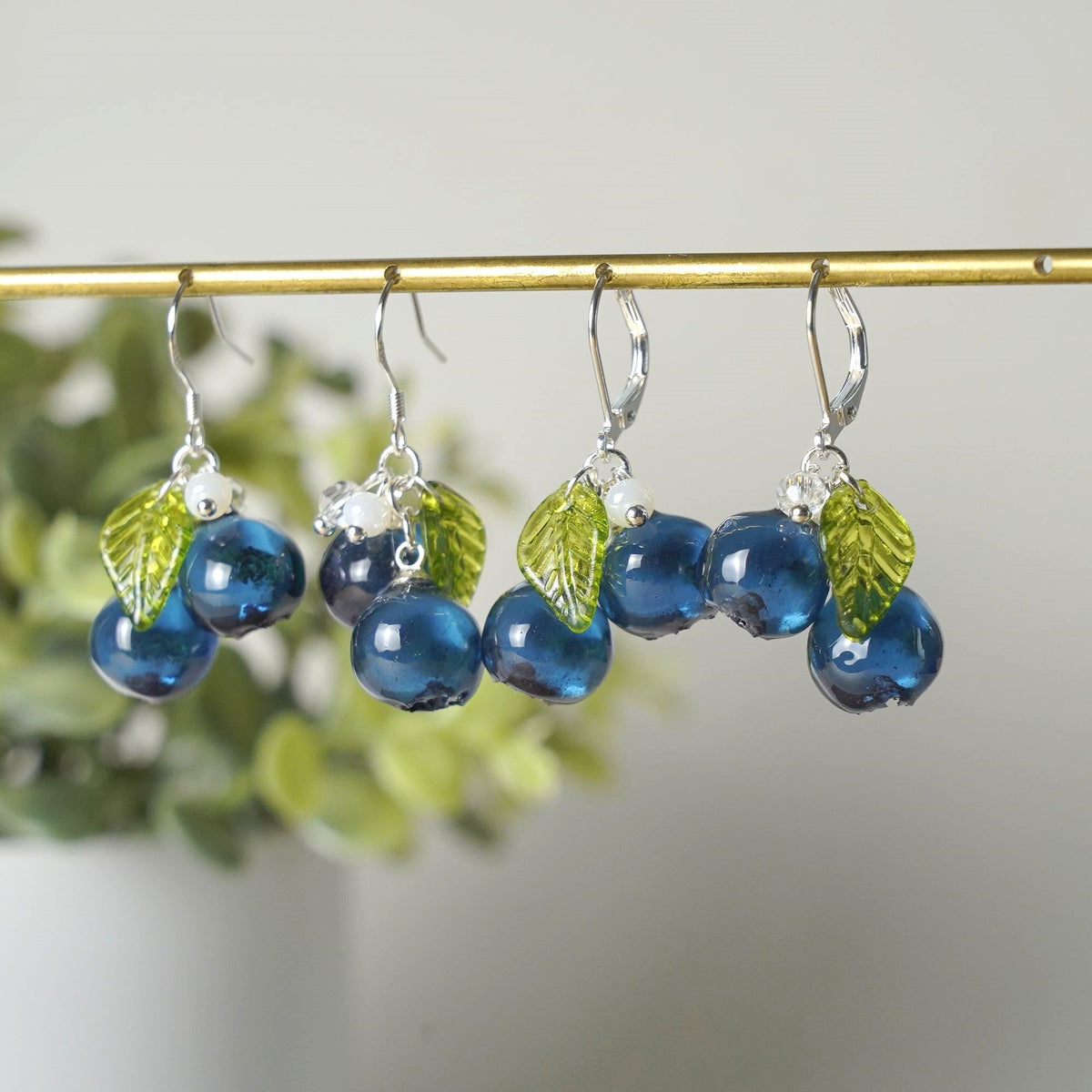 Blue resin blueberry cluster earrings set with green leaves on display hooks