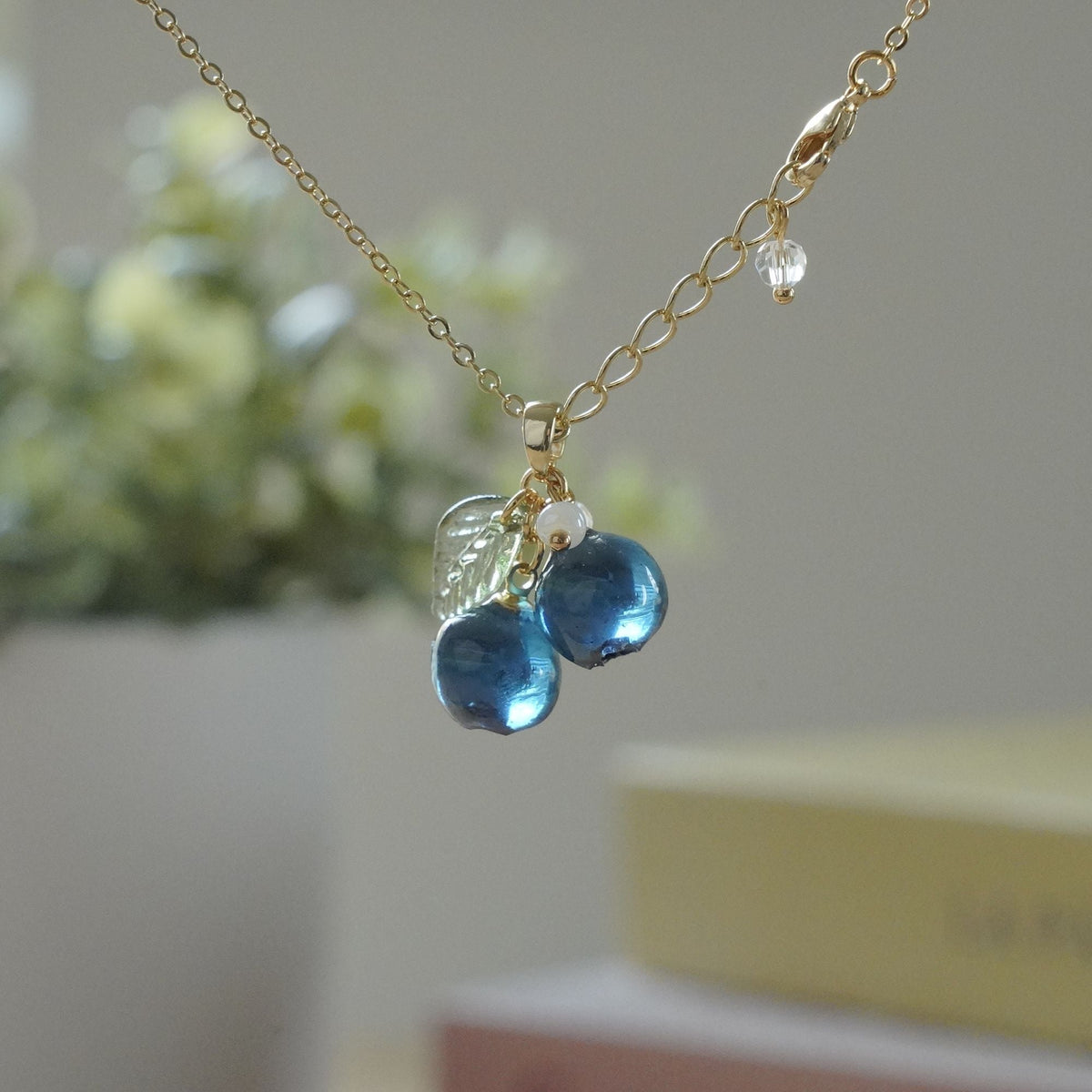 Gold blueberry cluster necklace with resin berries, green leaf accents, and small bead dangles