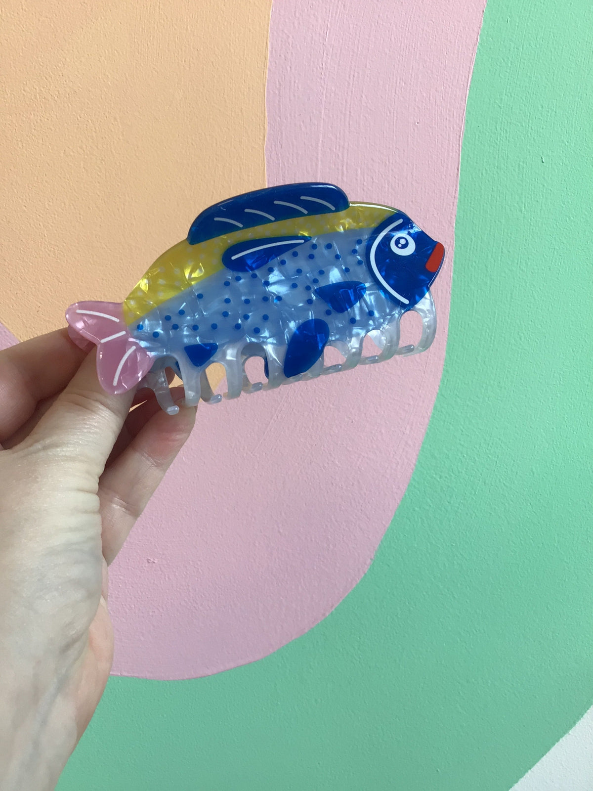 Blue fish hair claw with pink accents and speckled translucent comb teeth.