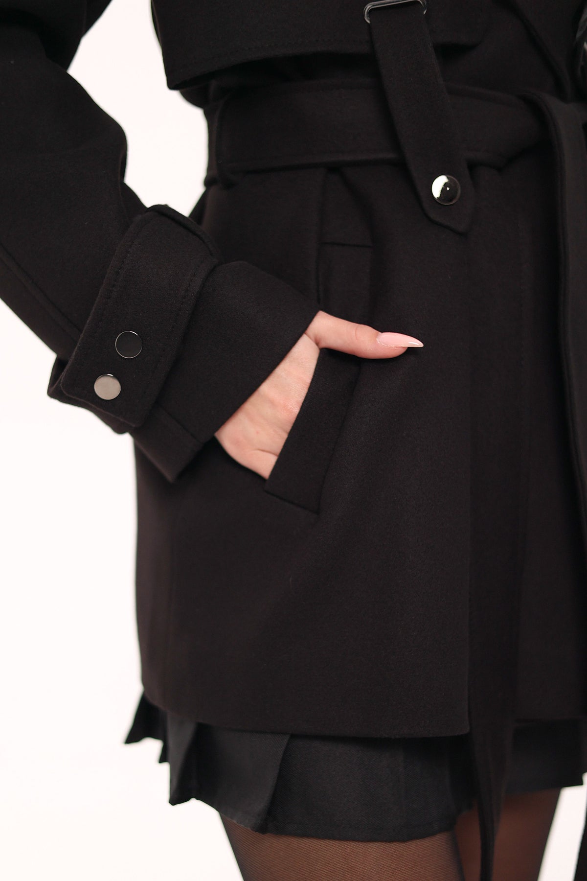 Close-up of the black coat's welt pocket, belt, and button-tab cuff.