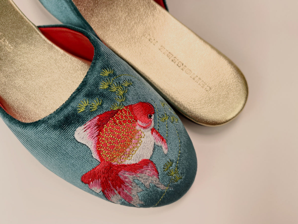 Teal velvet mule close-up with goldfish embroidery, red collar trim, beige sole