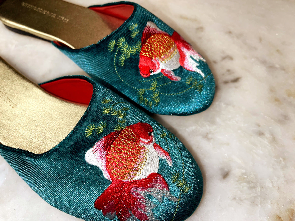 Close-up of teal velvet mule slippers with goldfish embroidery and red interior accents