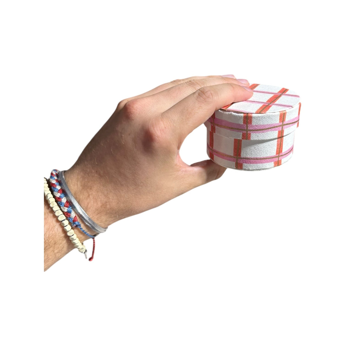 Hand holding a round handmade recycled paper gift box with red plaid stripes and lid.
