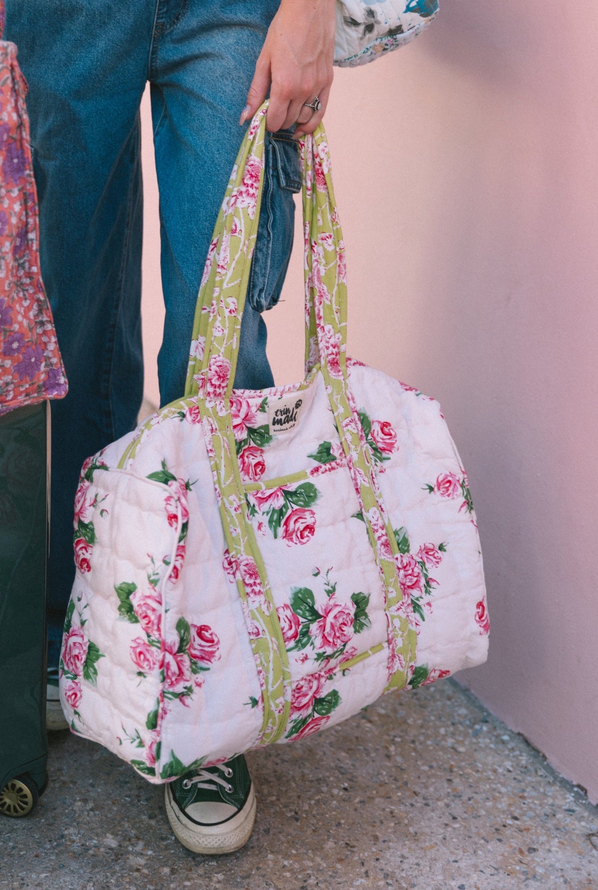Floral quilted duffle bag held by a shopper, pink roses with yellow-green straps