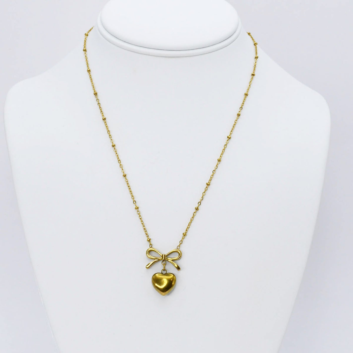 Gold bow and heart pendant necklace displayed on a mannequin