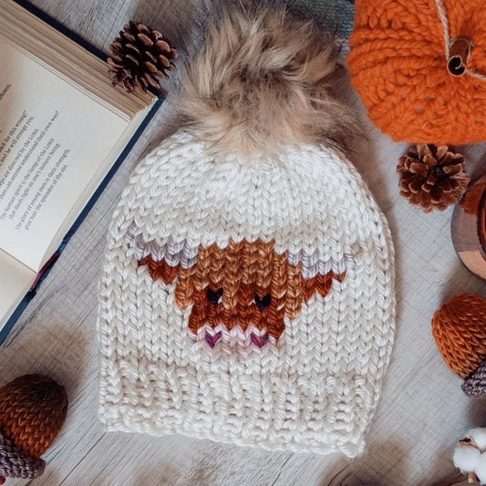 Cream knit beanie with faux-fur pom-pom and brown cow stripe design