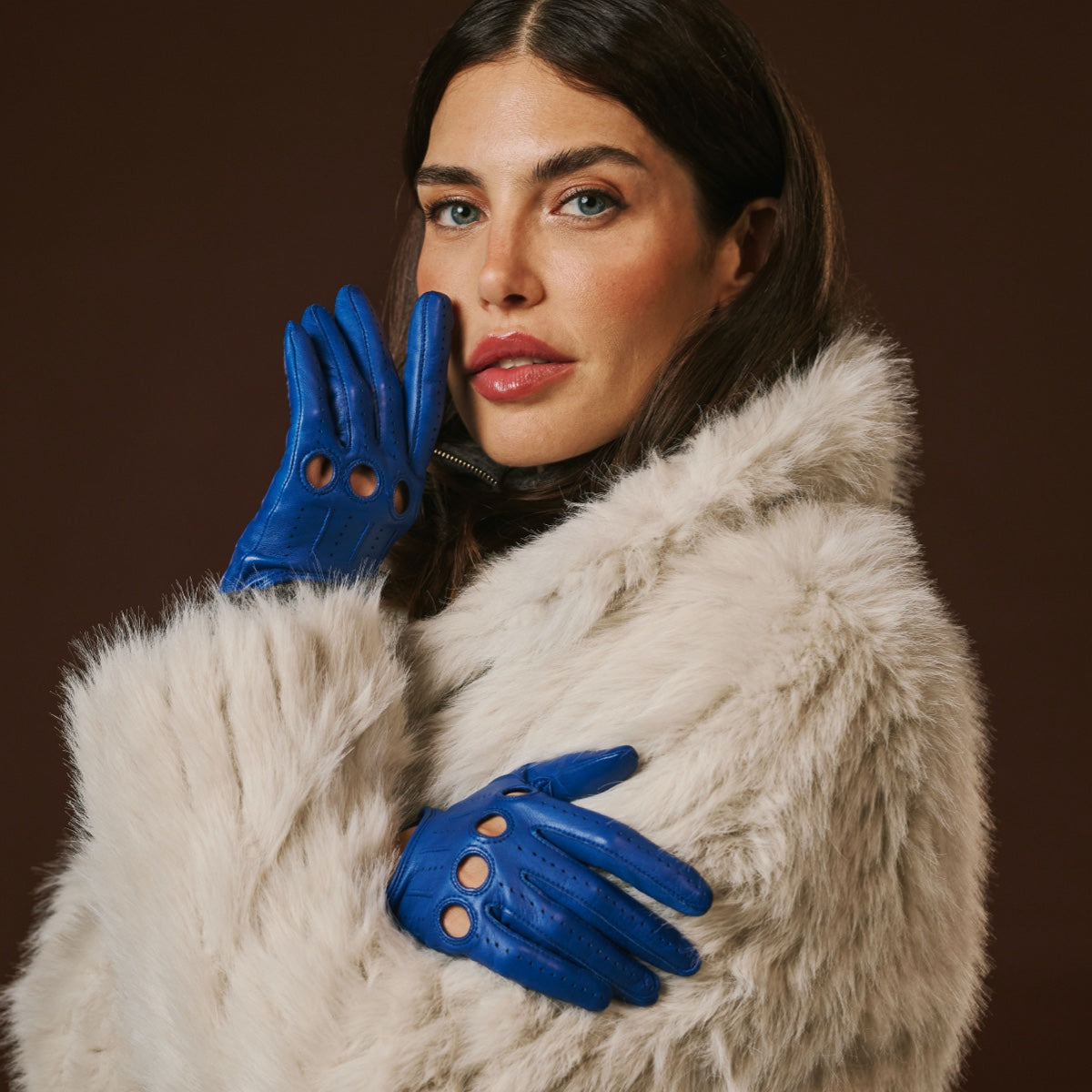 Blue leather driving gloves held to the chest, perforated detailing visible