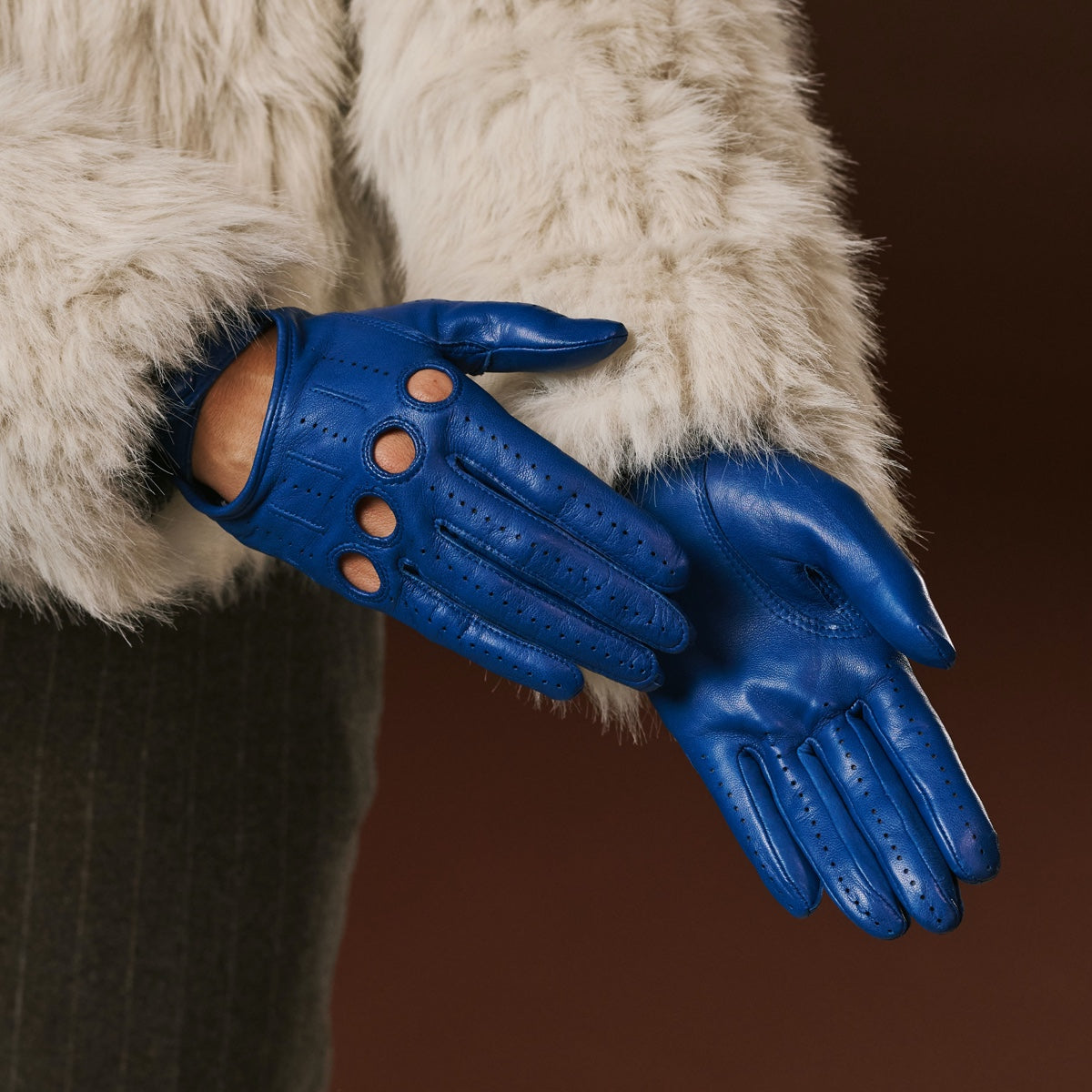 Close-up of blue leather driving gloves with circular cutouts and stitched seams