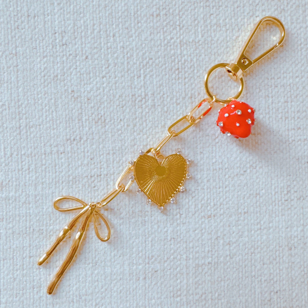 Gold bag charm with red strawberry bead, heart and fan charms, and bow tassel
