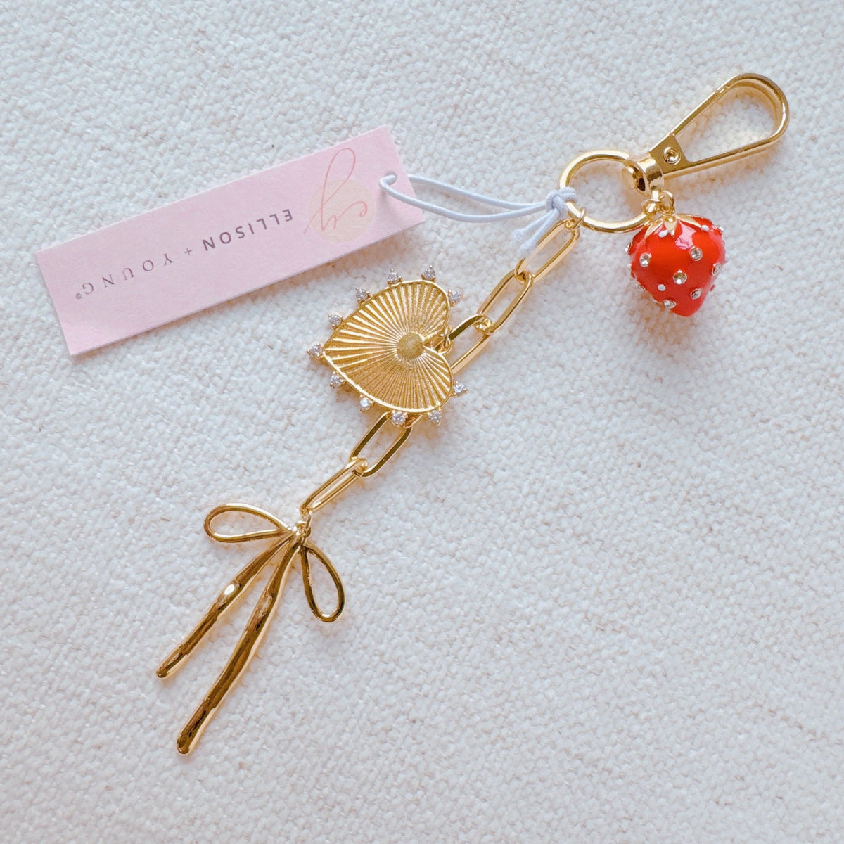 Gold bag charm with red strawberry bead, heart and fan motifs, and bow details
