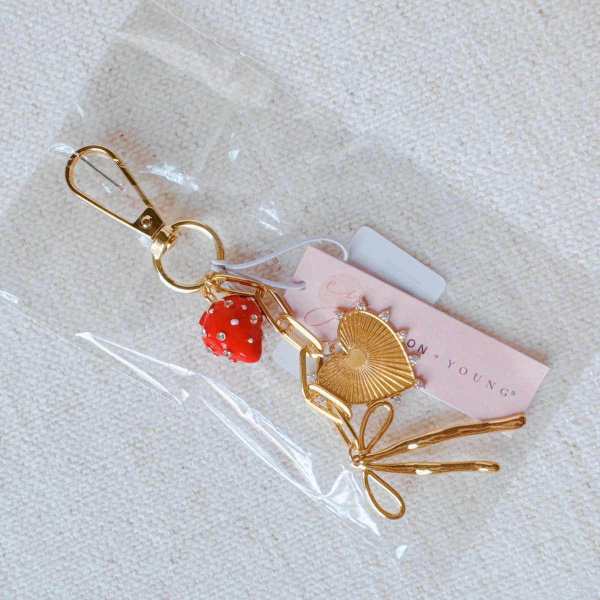 Gold bag charm with red strawberry bead and heart/fan charms on clear packaging