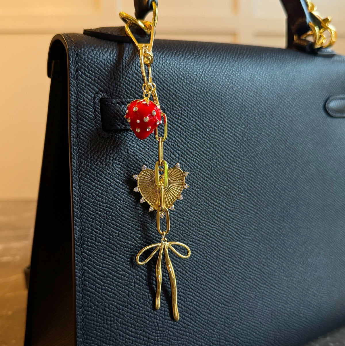 Gold bag charm with red strawberry bead, heart pendant, and dangling bow charms