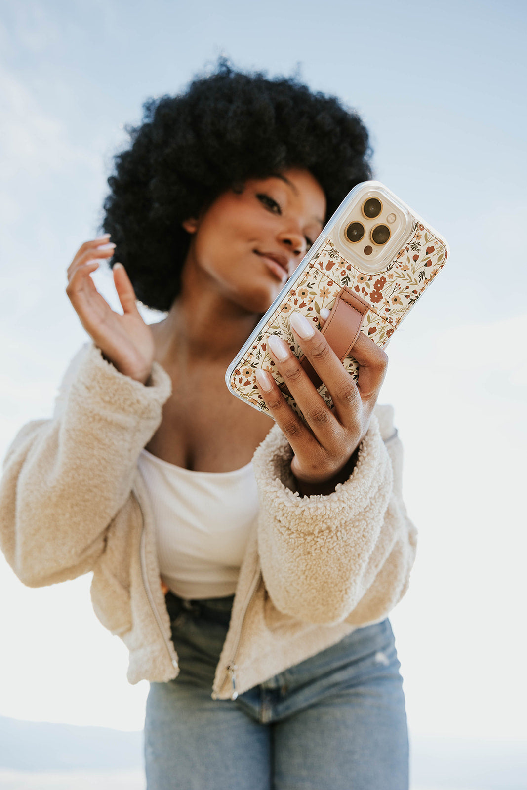Floral phone case with brown strap on smartphone, held by a woman