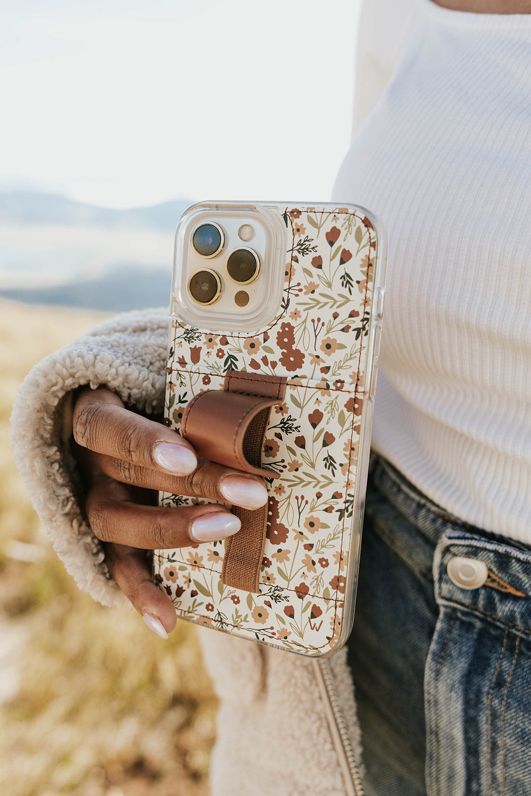 Floral phone case with brown wrist strap and clear back, close-up