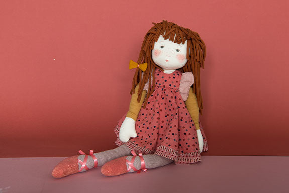 Seated Anemone rag doll wearing a pink polka-dot dress, gray tights, and ribbon shoes