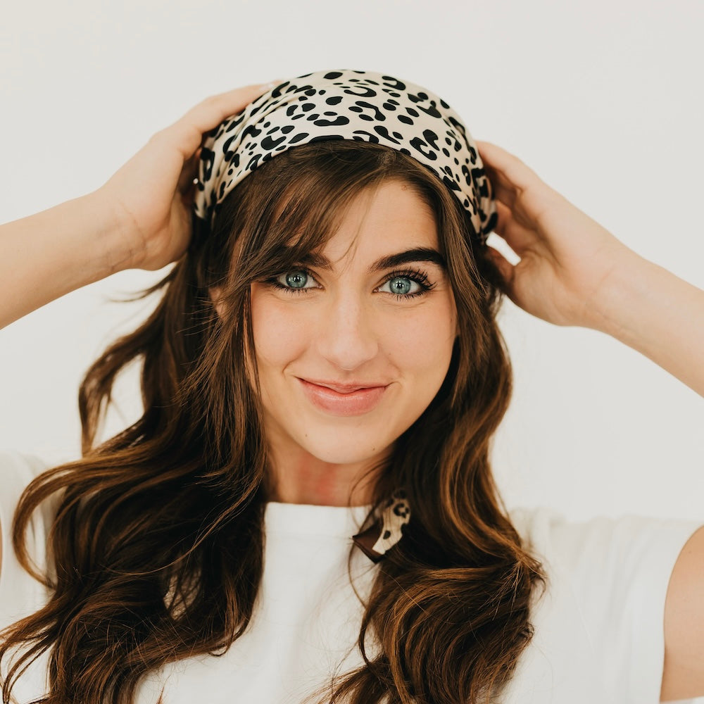 Leopard print square scarf with brown border, worn as a head scarf