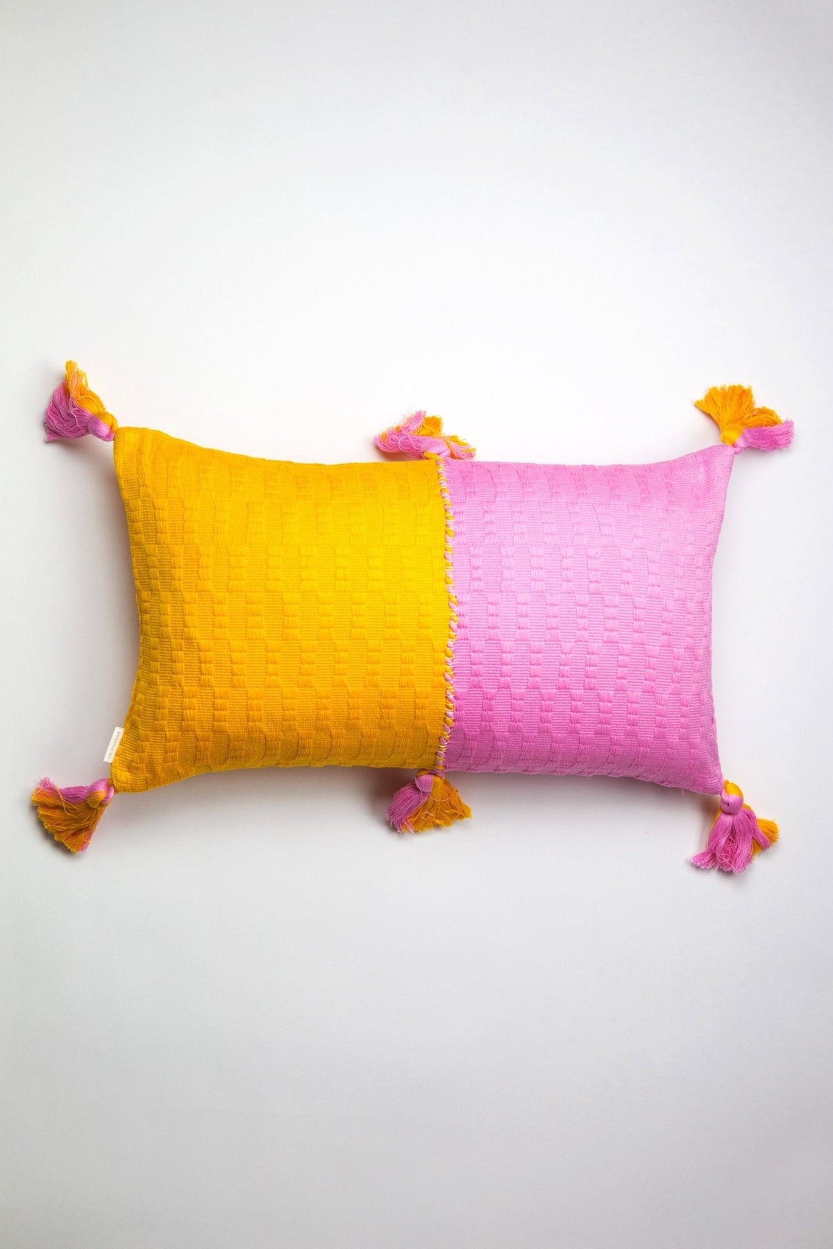 Two-tone yellow and pink throw pillow with textured weave and tassel corners