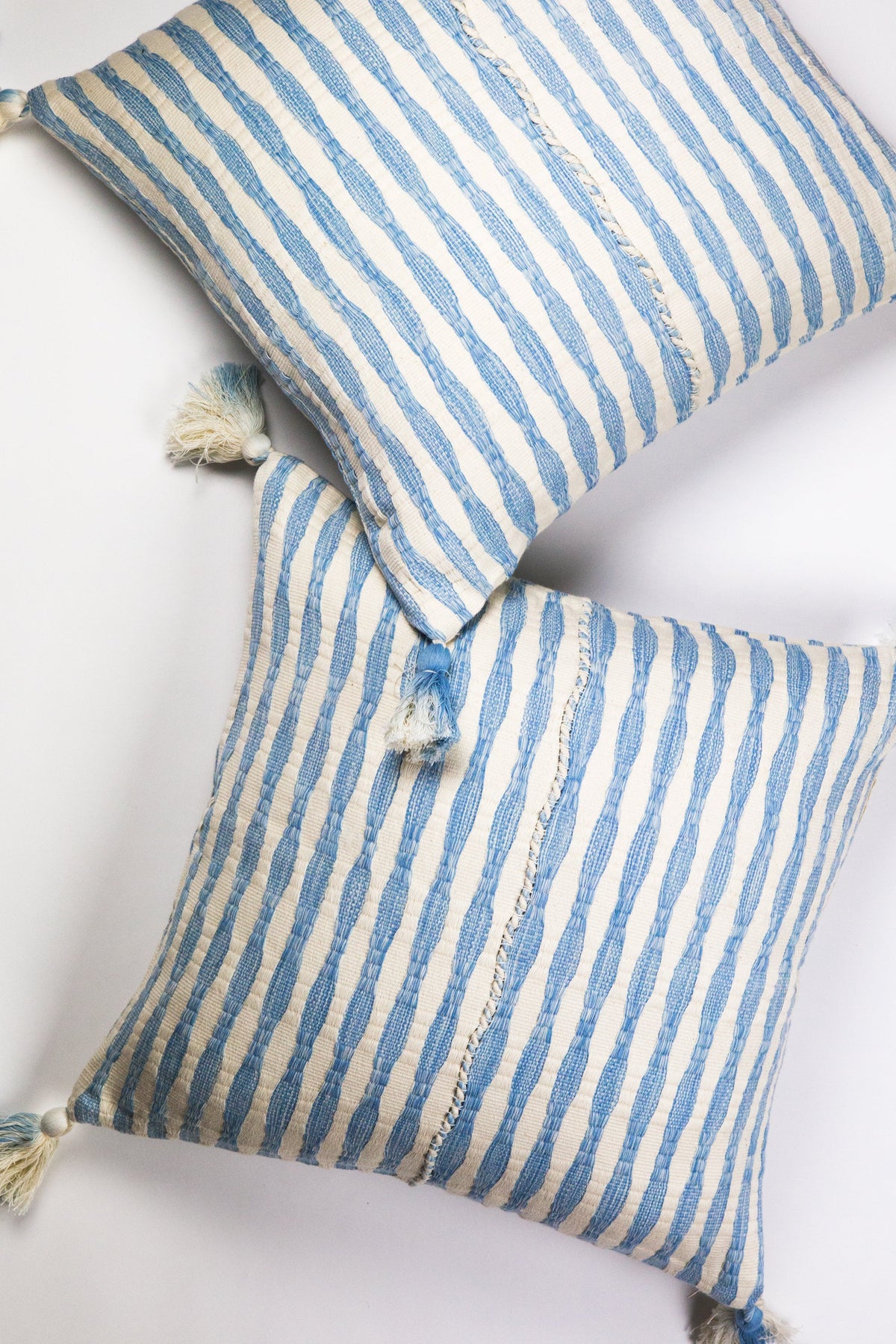 Folded view of blue striped pillows with corner tassels and ties