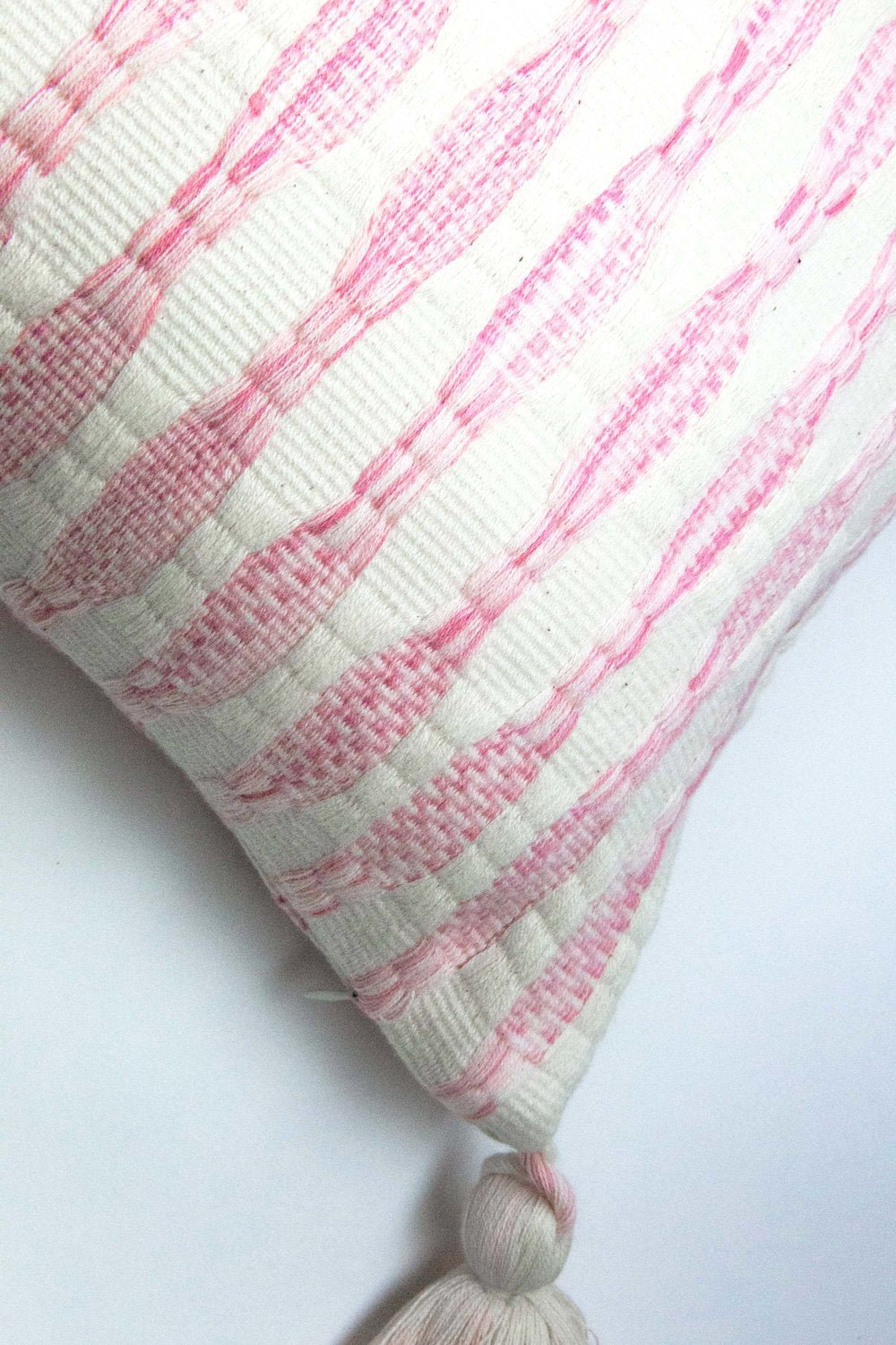 Close-up: faded pink vertical stripes on a striped pillow with tassel corners
