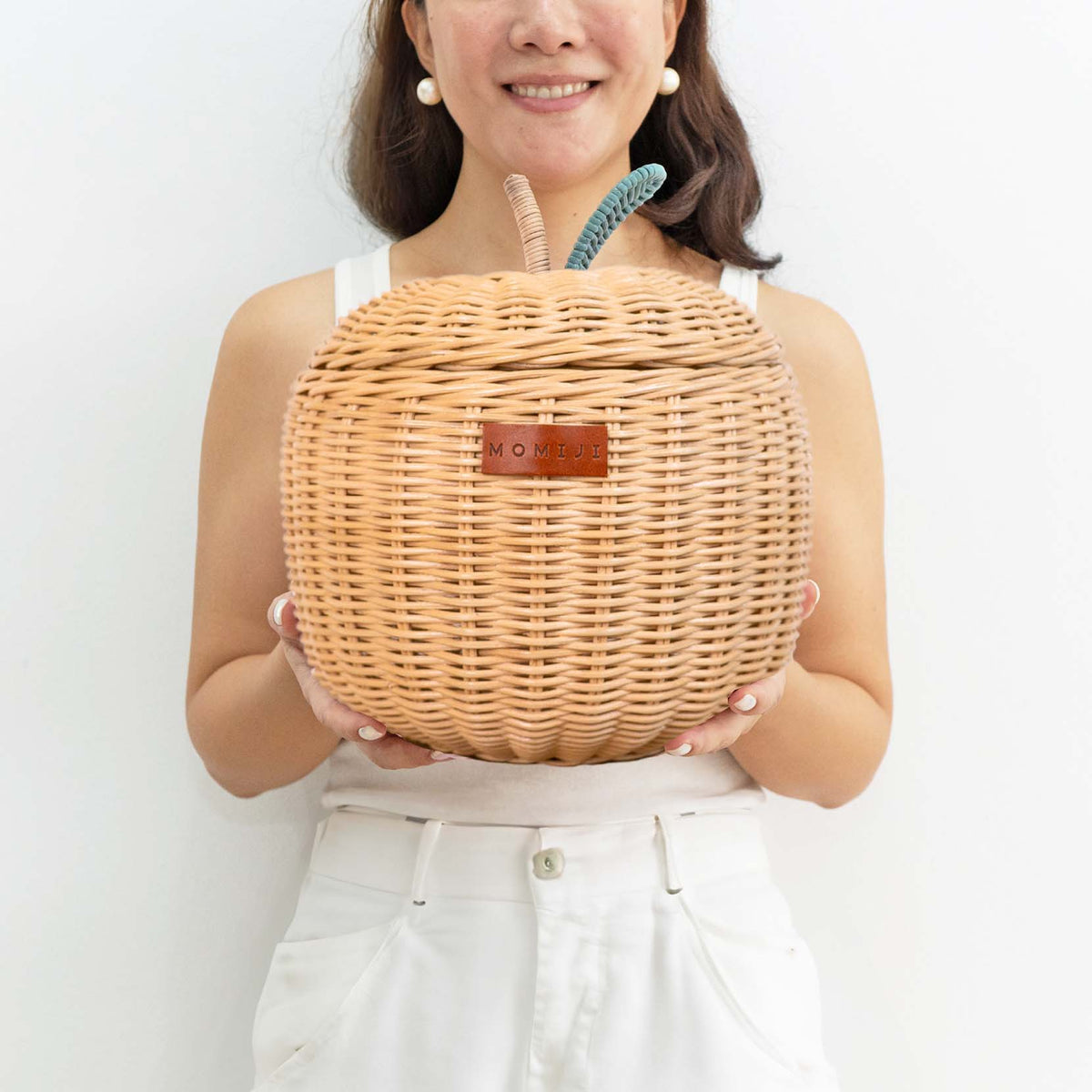 Small natural rattan apple basket with woven lid and teal leaf detail, held in two hands
