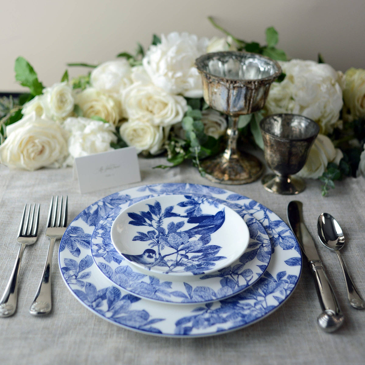 Blue botanical porcelain plate on table with silverware; white center with blue motif