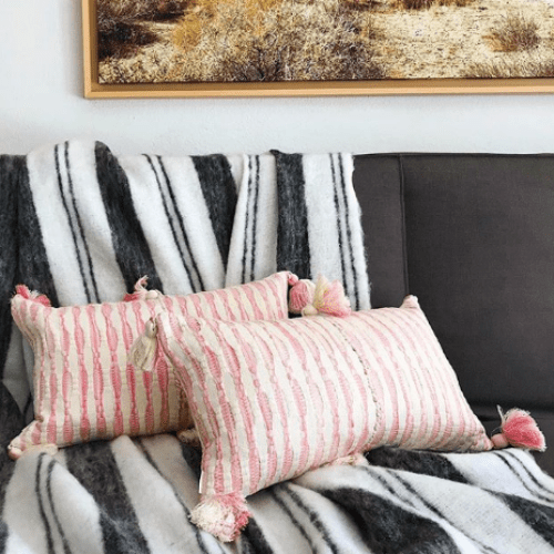 Faded pink striped pillows with corner tassel pom-poms on a sofa