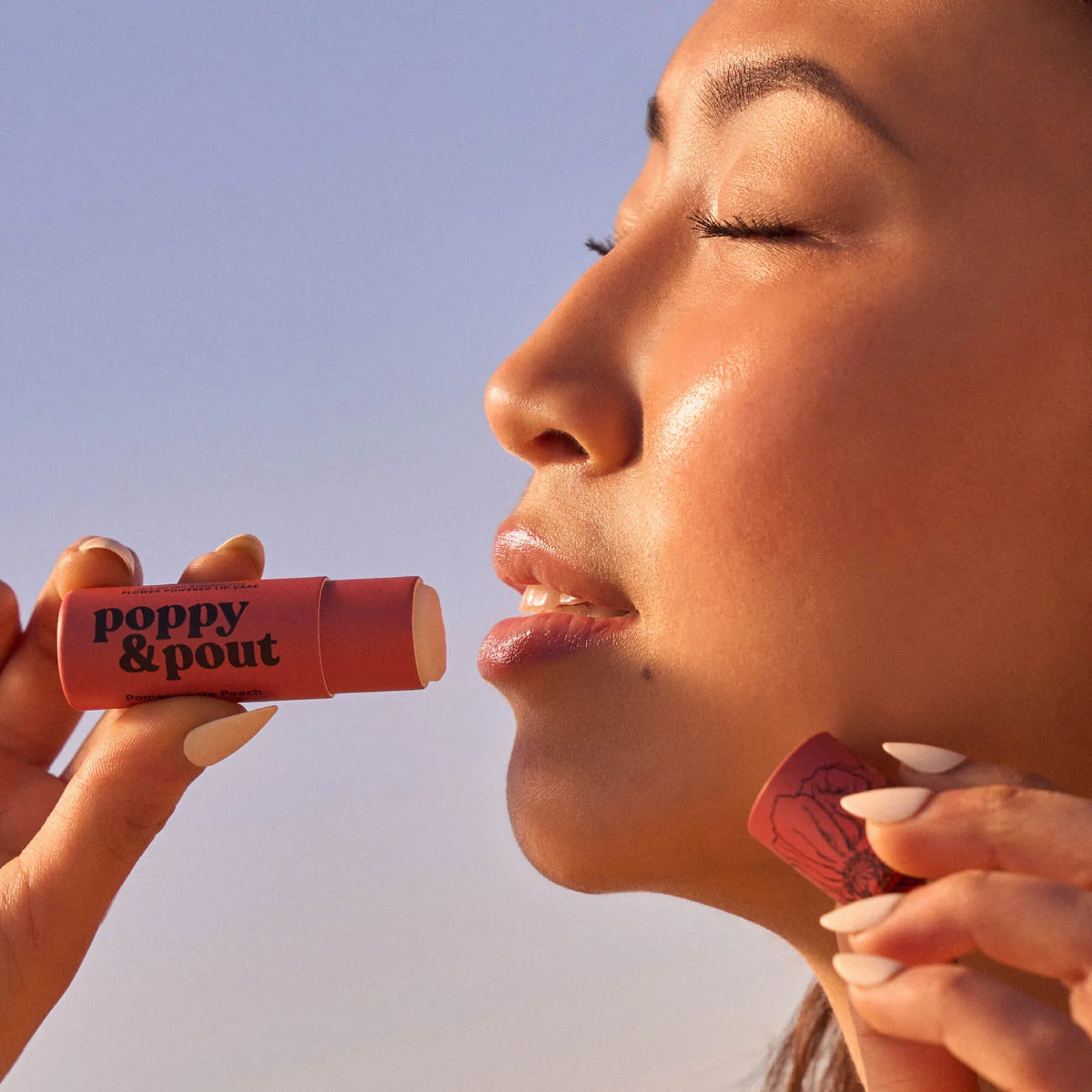 Pomegranate peach lip balm being applied on lips, with balm tube in hand
