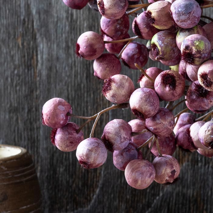 Close-up faux hawthorn berries in dusty purple and pink on branching stem
