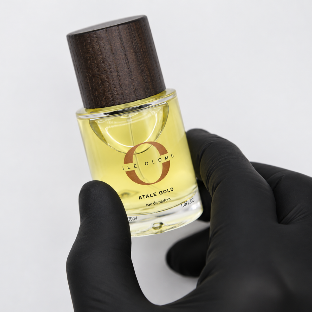 Eau de parfum bottle with dark wood cap held by black-gloved hand, 30 ml