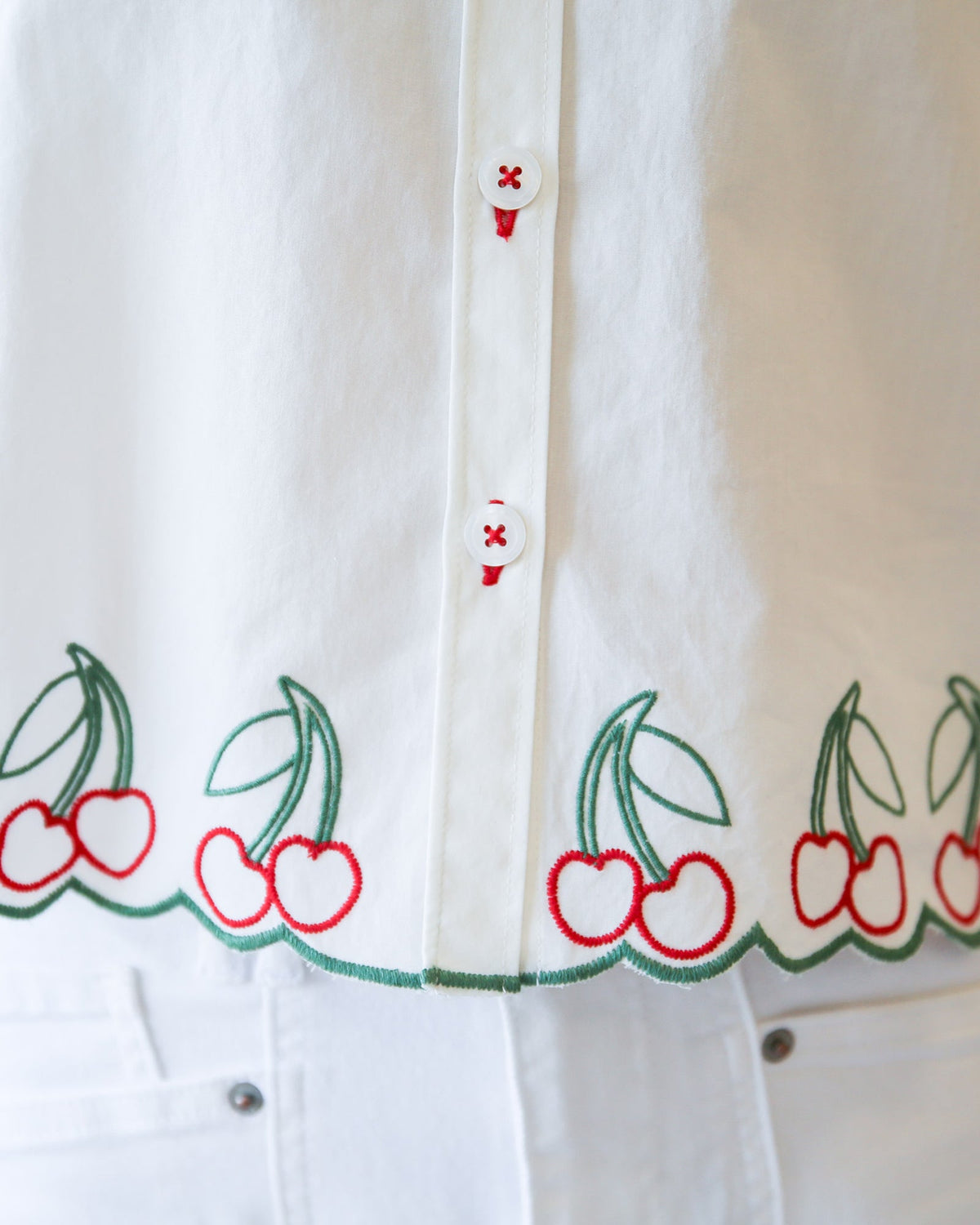 White shirt placket with red buttons and cherry-and-leaf hem embroidery