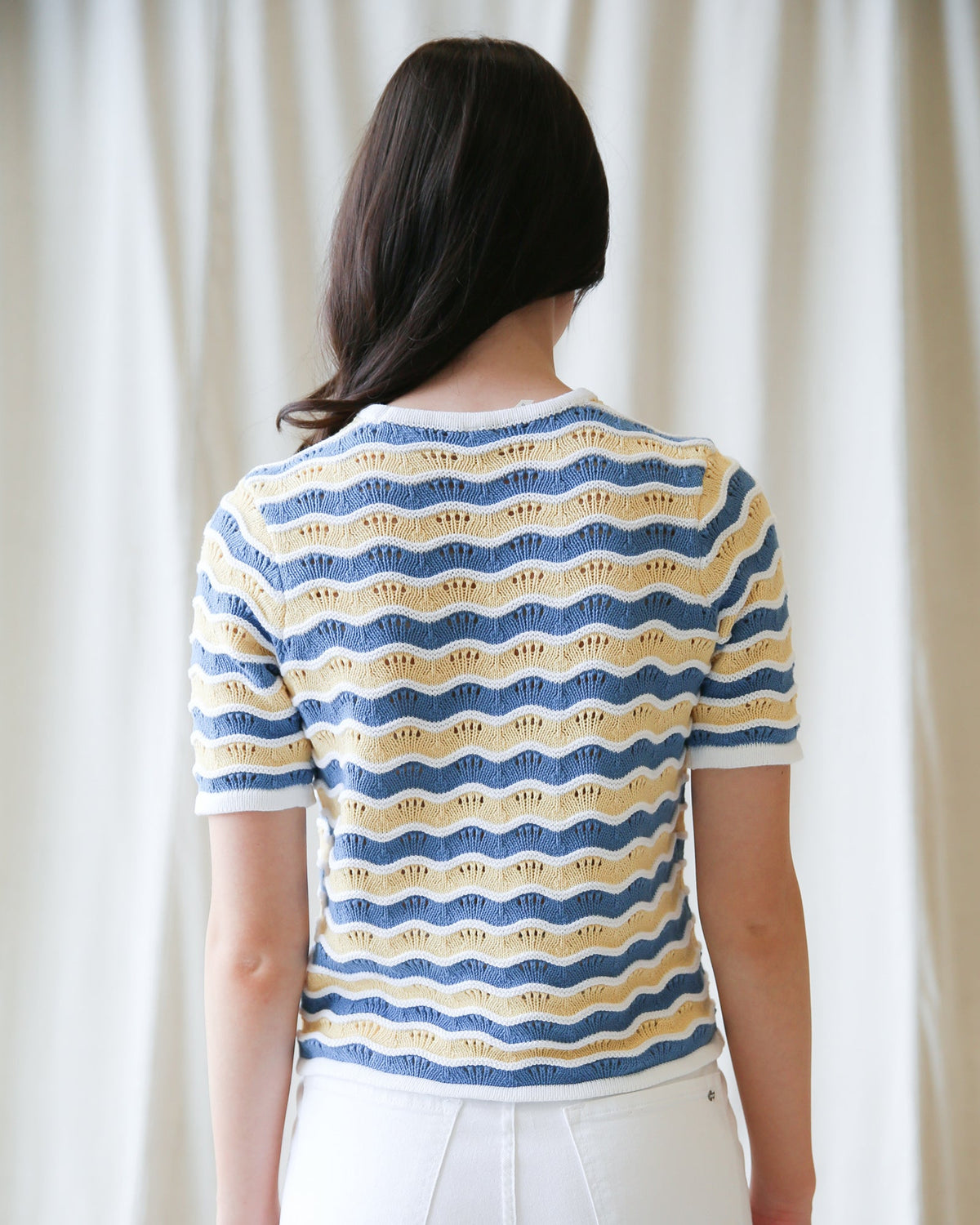 Back view of striped knit sweater with blue and yellow wavy bands, short sleeves